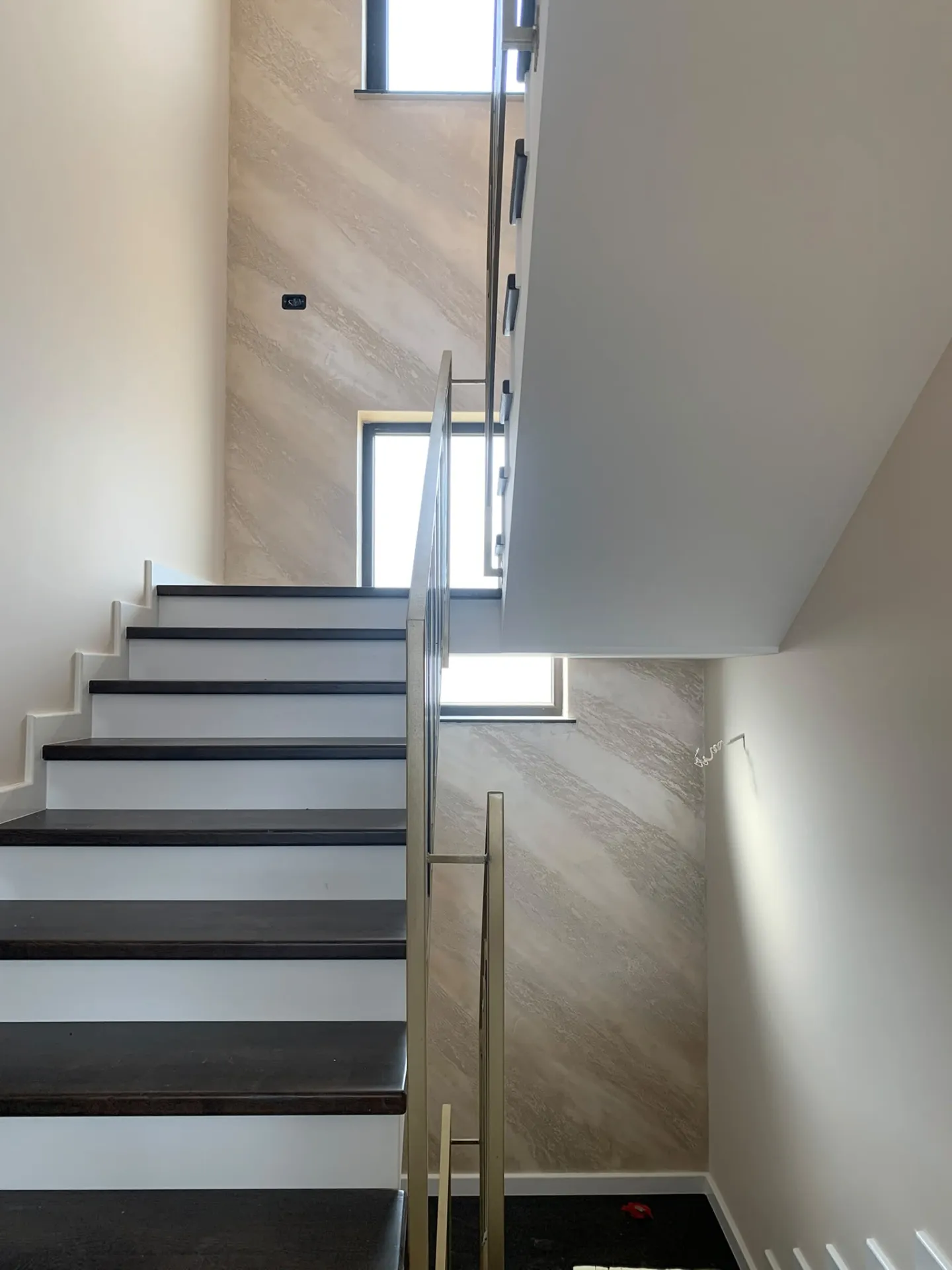 Vedere ascendentă pe casa scării cu finisaje travertin și balustradă modernă